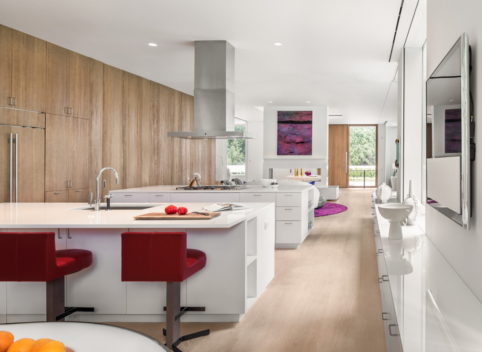 Open kitchen with white countertops and wood cabinetry, accented by red barstools and contemporary lighting, seamlessly connecting to dining and living areas.