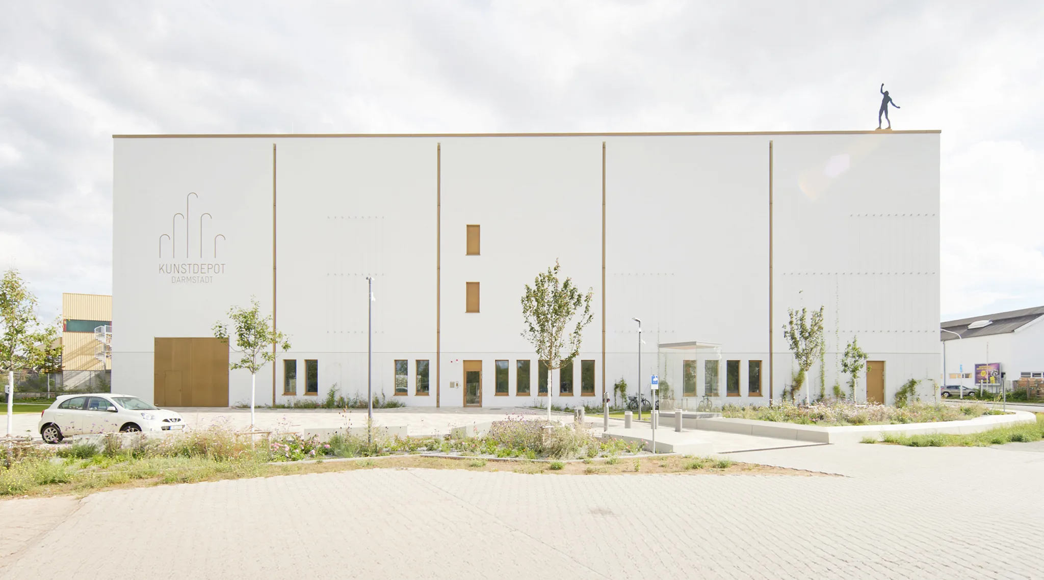 Darmstadt Art Depot—minimal white facade with sparse, wood-trimmed openings and a landscaped forecourt