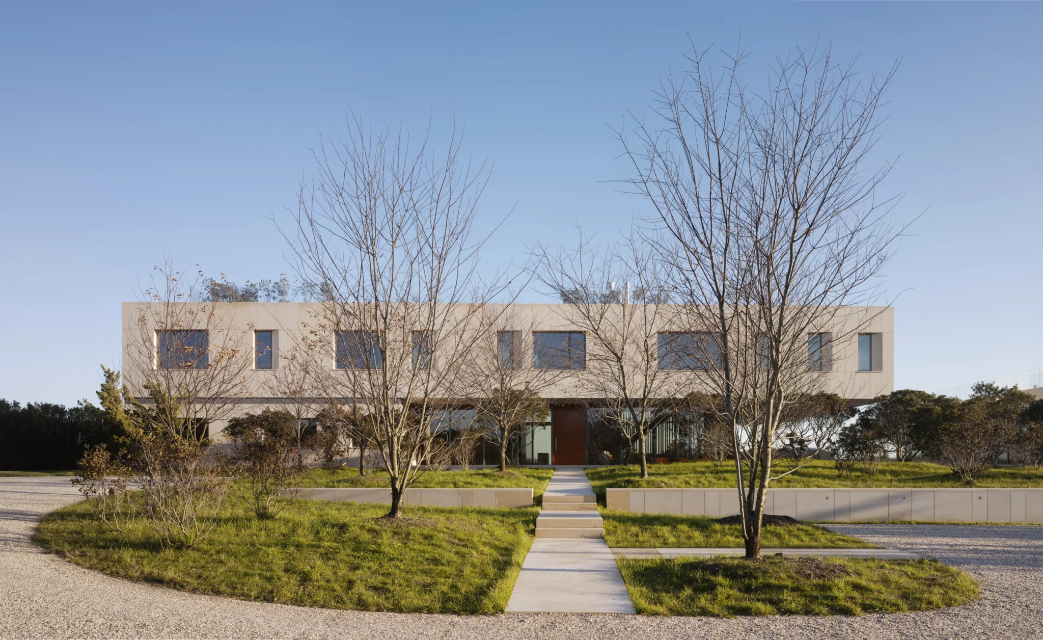 Contemporary coastal residence with rectangular upper volume, landscaped approach, and clean geometric design in natural tones.