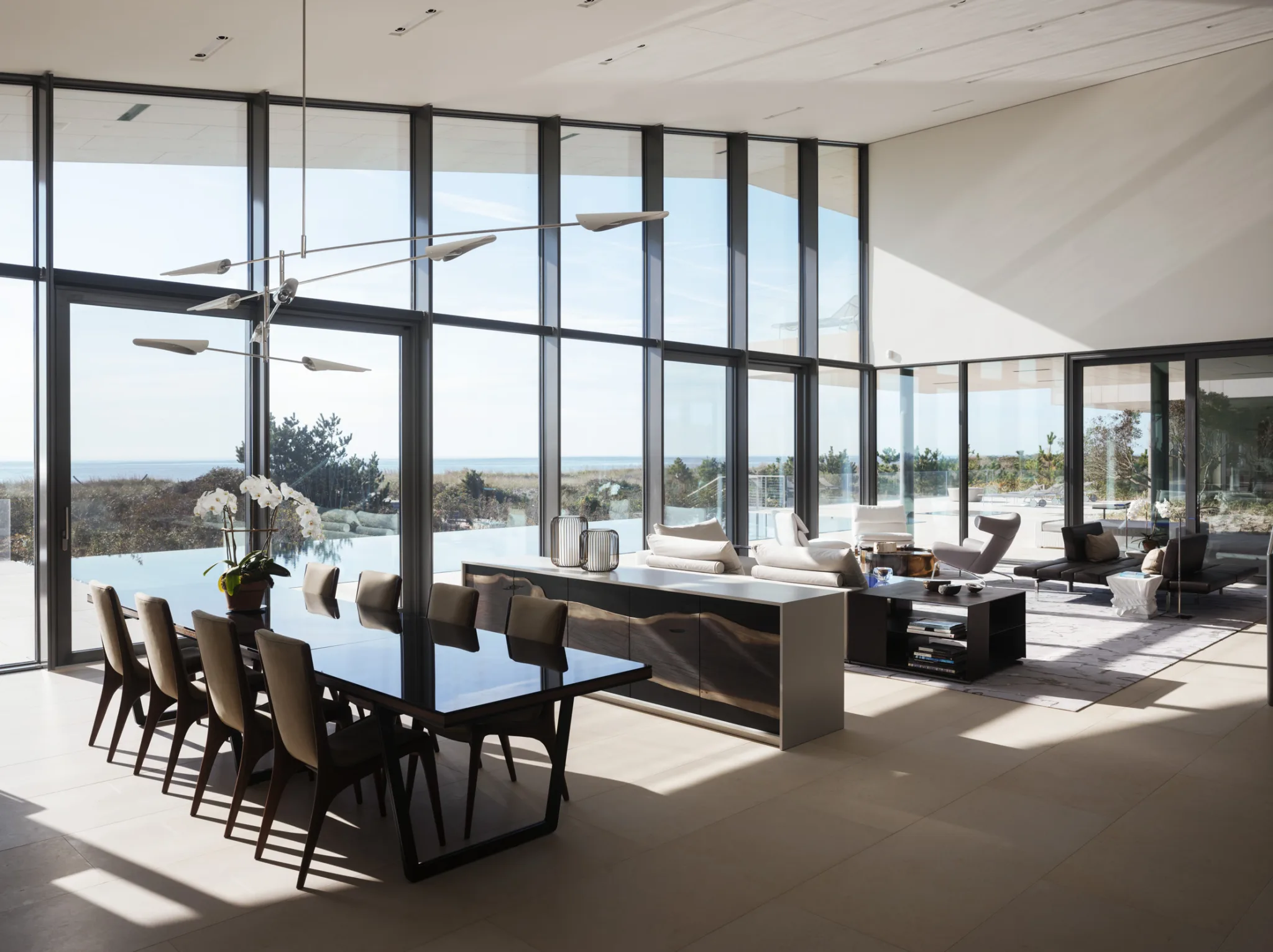 Open-plan living and dining area with panoramic ocean views, glass walls, and contemporary furnishings connecting to the outdoor terrace.