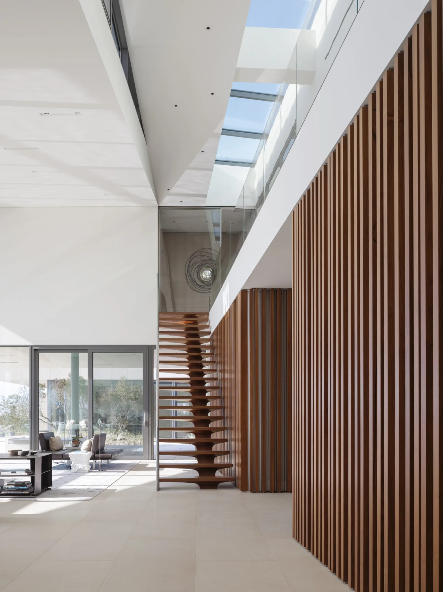 Double-height entryway with glass skylights, vertical wood slats, and floating staircase enhancing natural light and spatial flow.