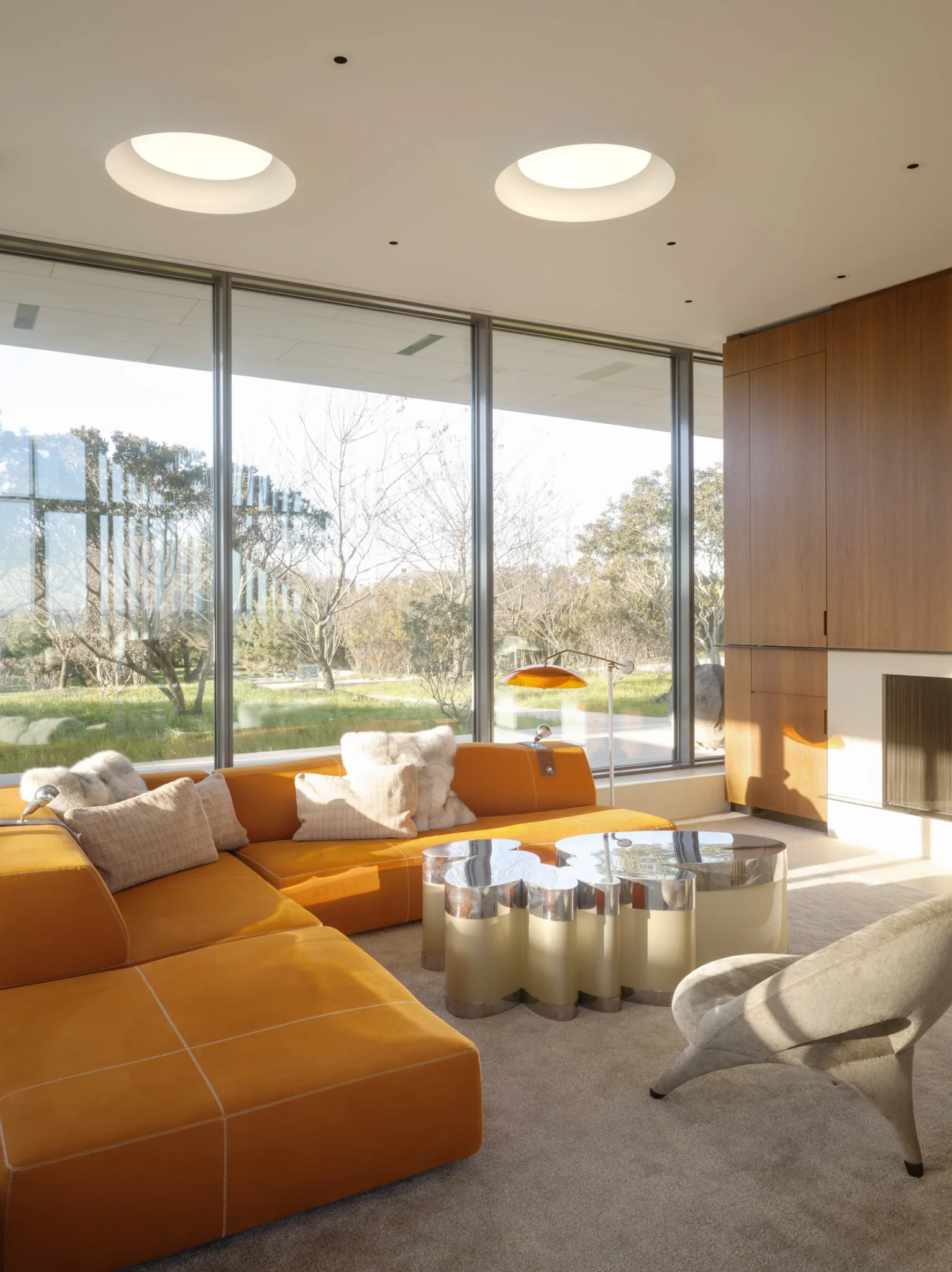 Bright living room with circular skylights, floor-to-ceiling windows, and a bold orange sectional sofa creating a warm modern aesthetic.