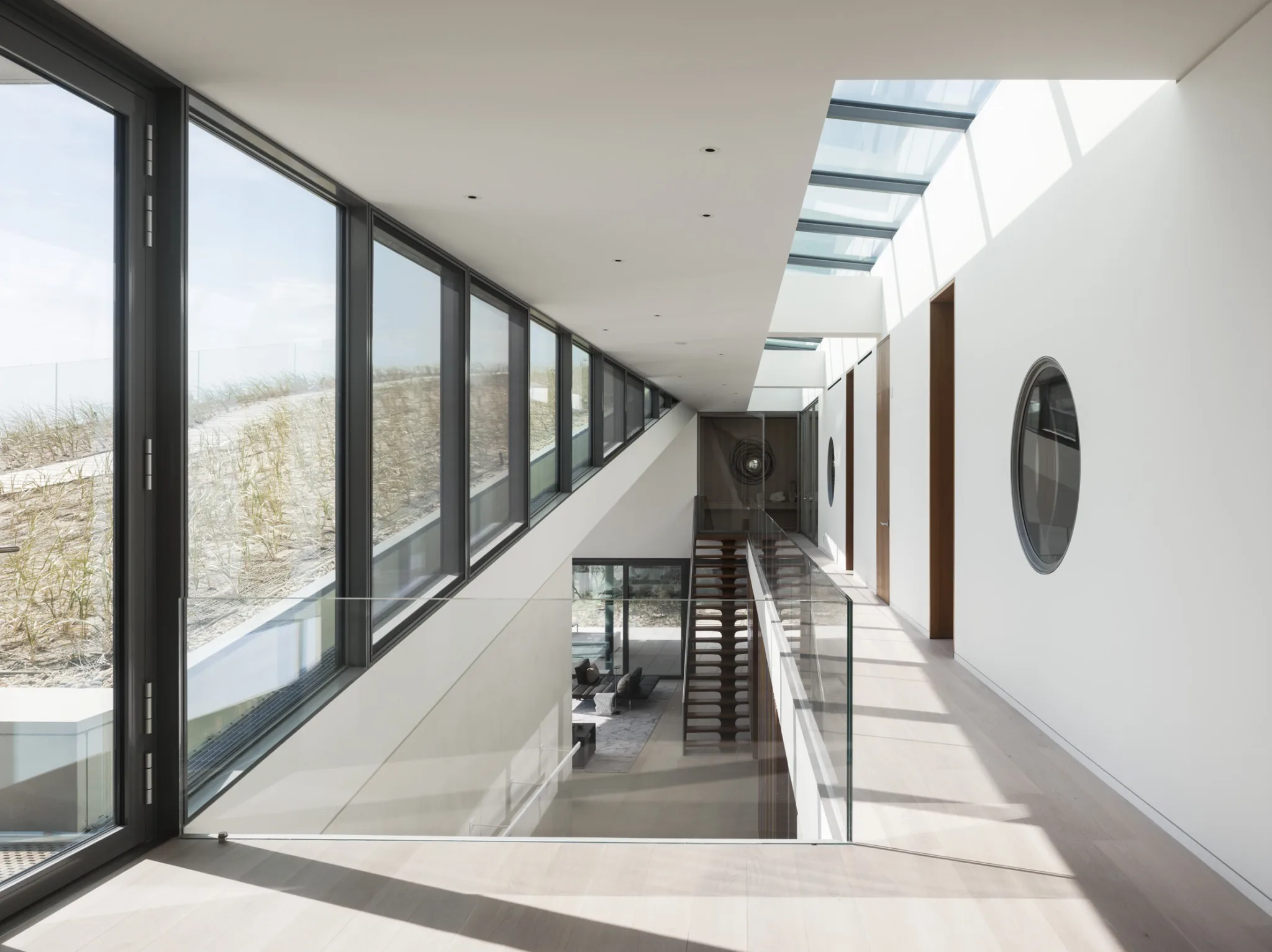 Upper-level corridor with skylights and glass railing overlooking open living areas and the home’s green roof.