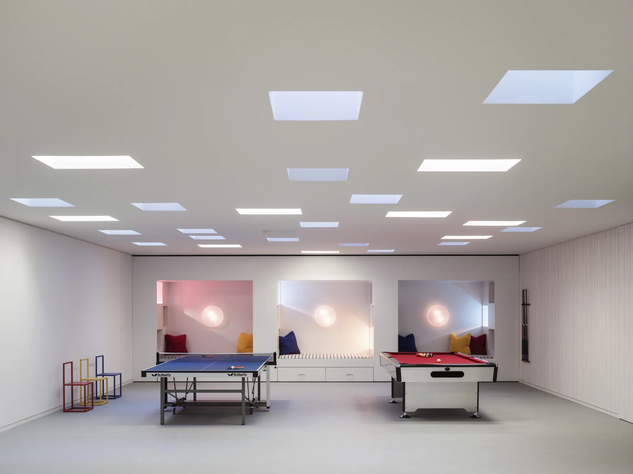 Recreation room with ping pong and air hockey tables, skylights, and built-in seating illuminated by soft colored lighting.