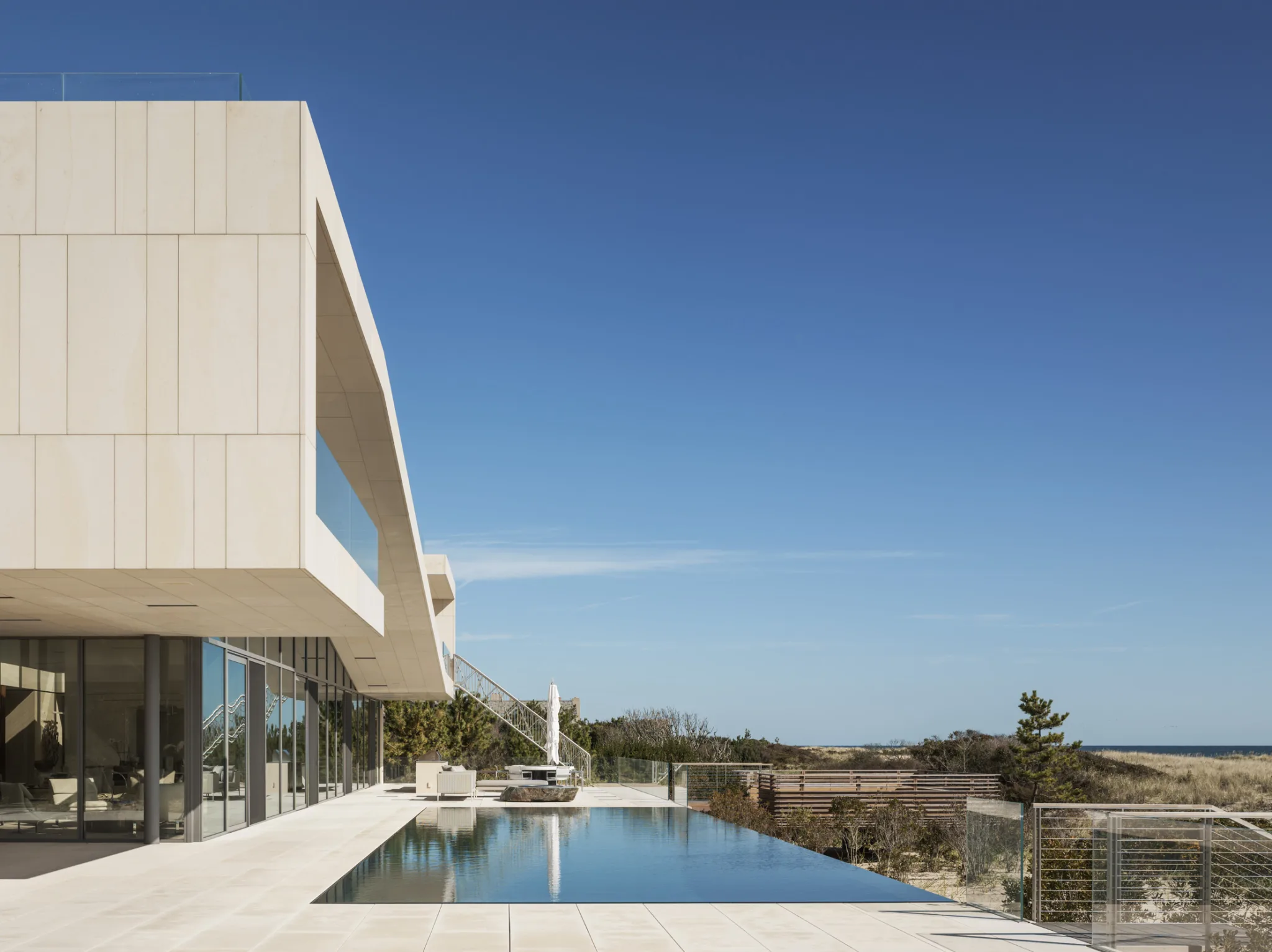 Expansive beachfront terrace with infinity pool and panoramic ocean views, framed by minimalist modern design.