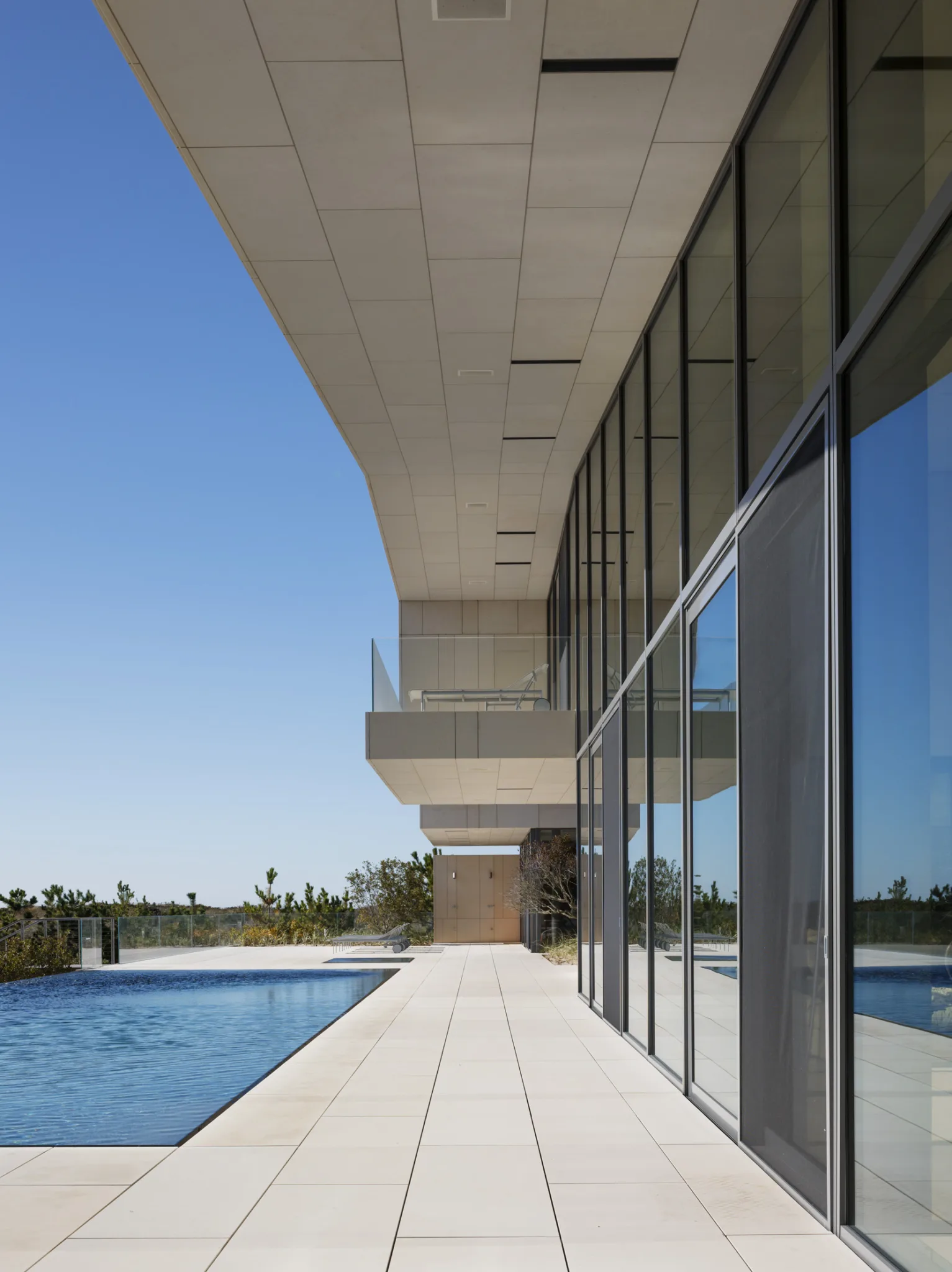 Glass-walled corridor overlooking the pool and beach, showcasing cantilevered architecture and oceanfront views.