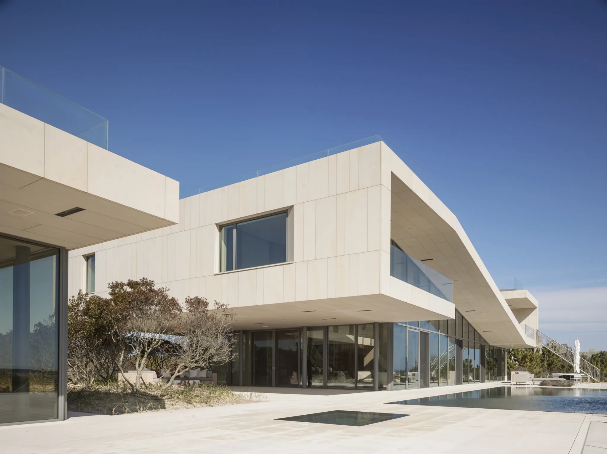 Modern coastal home with angular stone façade, large windows, and pool terrace blending with the surrounding dune landscape.