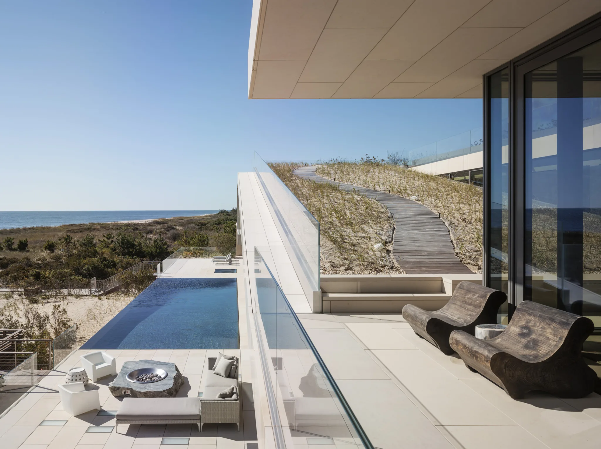 Contemporary coastal residence with infinity pool, dune-inspired green roof, and ocean-facing terrace featuring modern lounge seating.