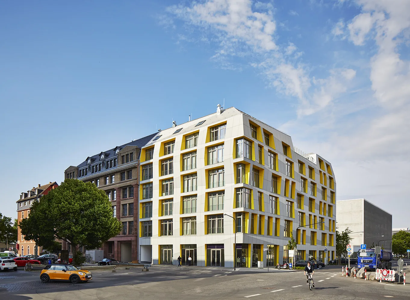 Corner perspective of the Main East Side Lofts, highlighting the angular white facade with recessed yellow accents, large windows, and integration into the historic urban fabric.