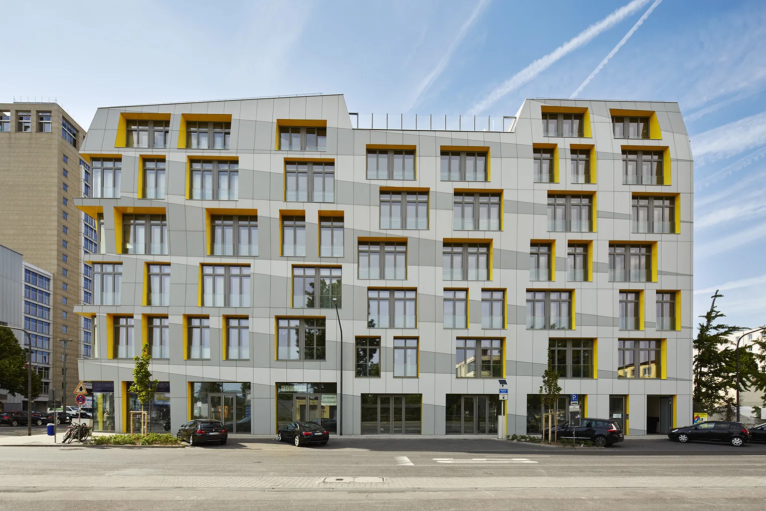 Street-facing view of the Main East Side Lofts, featuring a rhythmic facade of large windows with angled yellow insets set into a geometric white exterior.