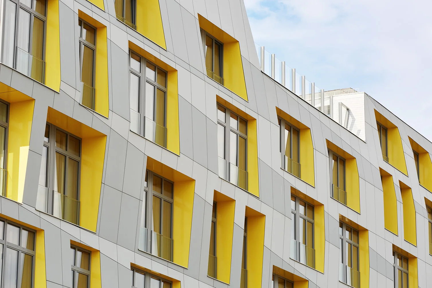 Close-up of East Side Lofts’ facade in Frankfurt, highlighting geometric window frames with bold yellow recesses that animate the gray exterior panels.
