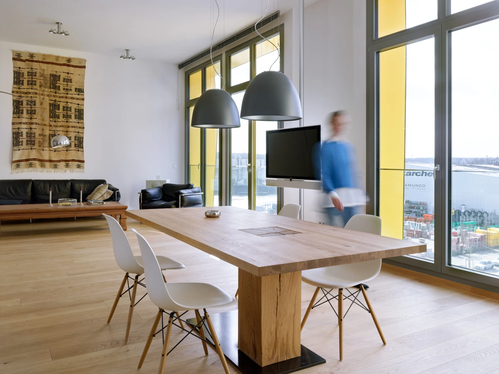 Bright loft living space with full-height windows, wood flooring, and a dining table overlooking the river at Main East Side Lofts.
