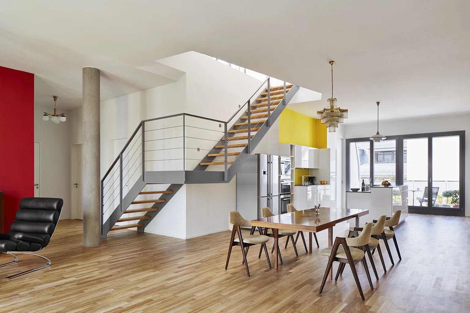 Open-plan loft interior with modern staircase, wooden floors, dining table, and bold accent walls in red and yellow at Main East Side Lofts.