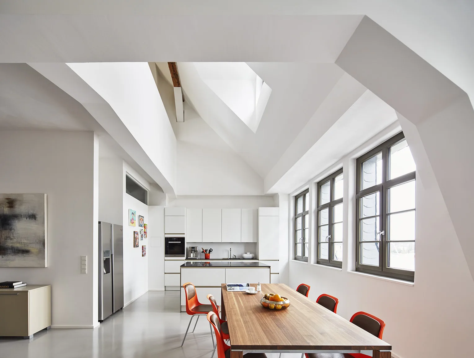 Bright loft kitchen with long wood dining table and orange chairs.