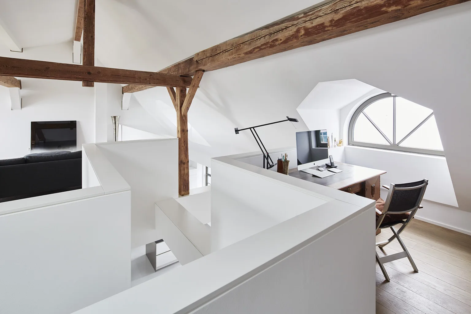 Modern loft workspace with angled ceiling, exposed beams, and arched window.