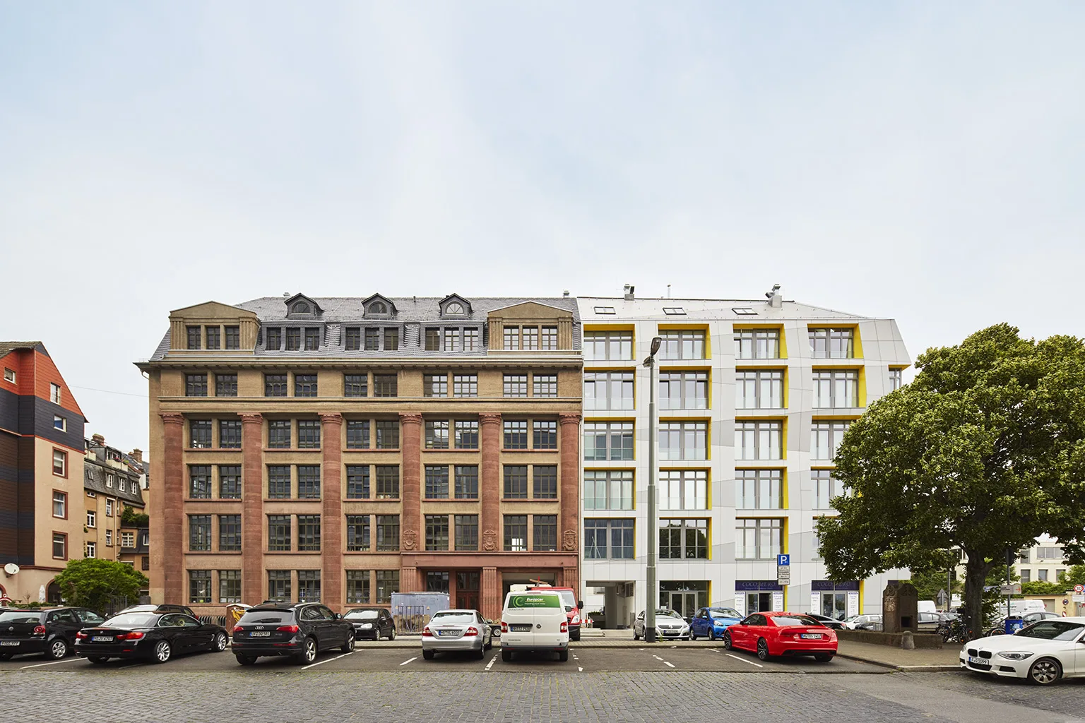 Main East Side Lofts exterior in Frankfurt by 1100 Architect, showing restored neoclassical red-brick façade alongside a modern folded cement-fiberboard addition with mansard roof and bold yellow window reveals.
