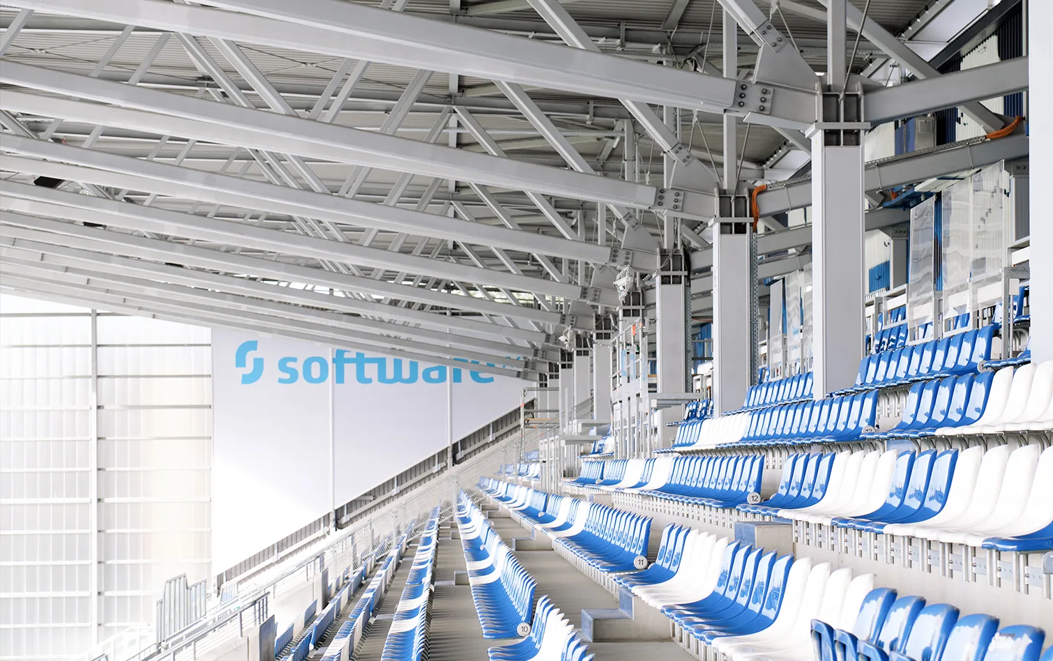 Rows of blue and white stadium seats beneath structural steel beams, creating a rhythm of lines and color.