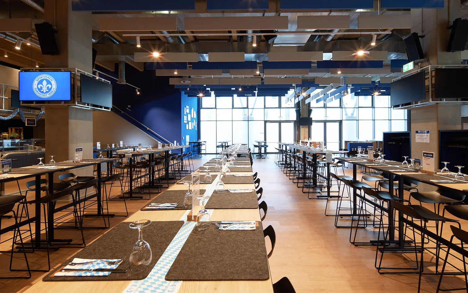 Hospitality hall inside the stadium featuring long tables, black chairs, and large windows letting in natural light.