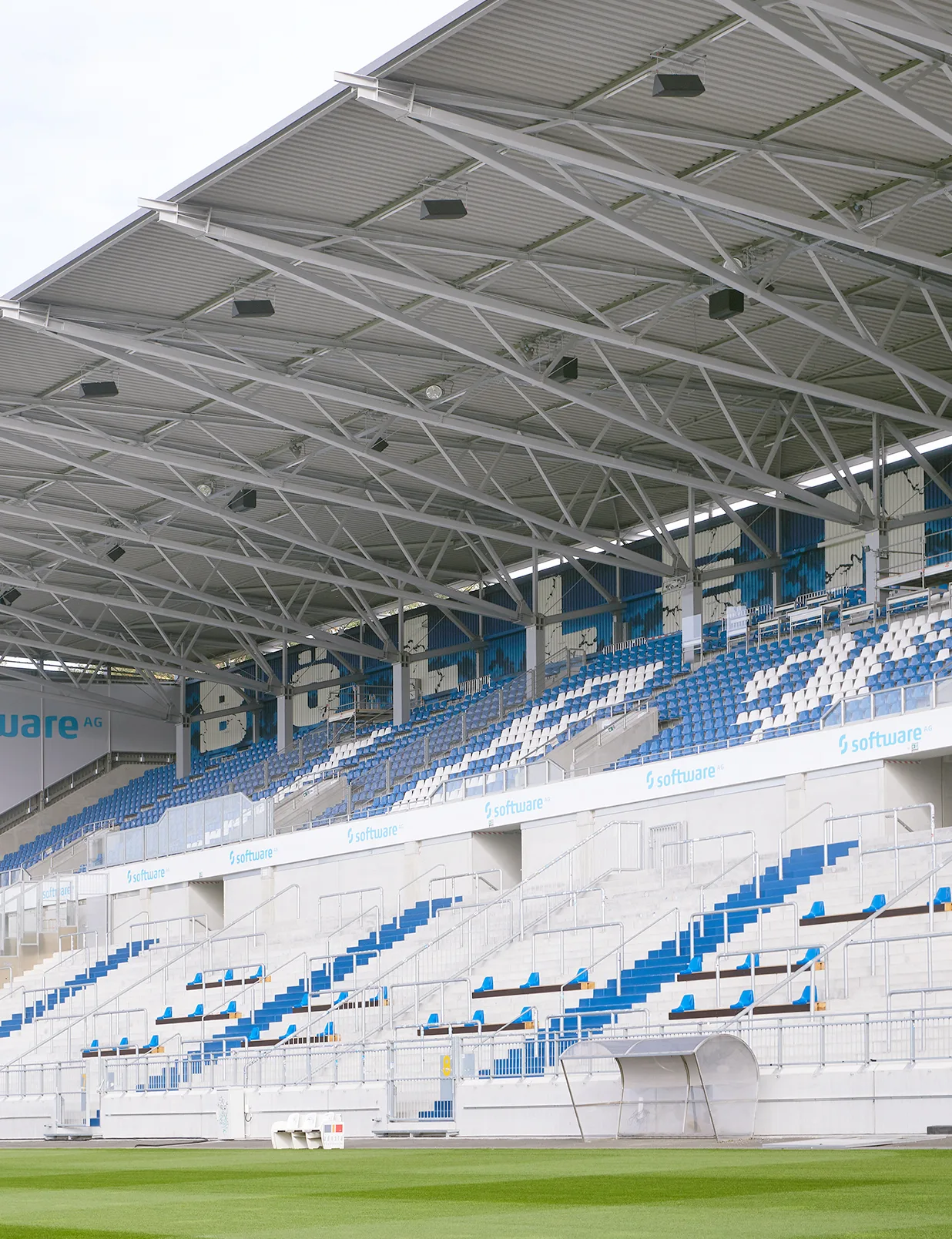 Covered seating section with blue and white patterned seats and structural steel roof trusses.