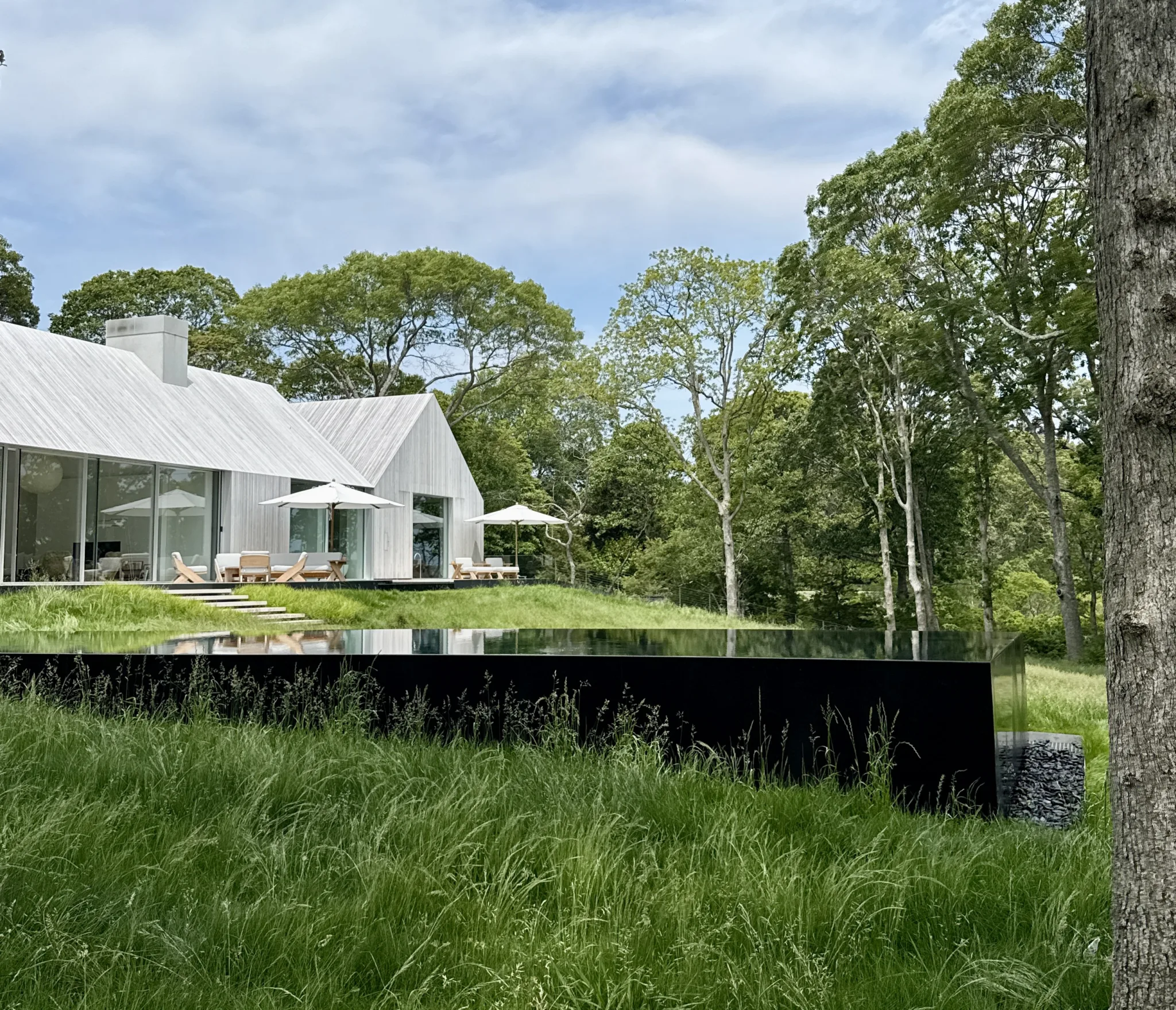 Sag Harbor waterfront house by 1100 Architect for Kelly Klein, featuring two perpendicular barn-like volumes and lush lawn leading to Sag Harbor Bay.