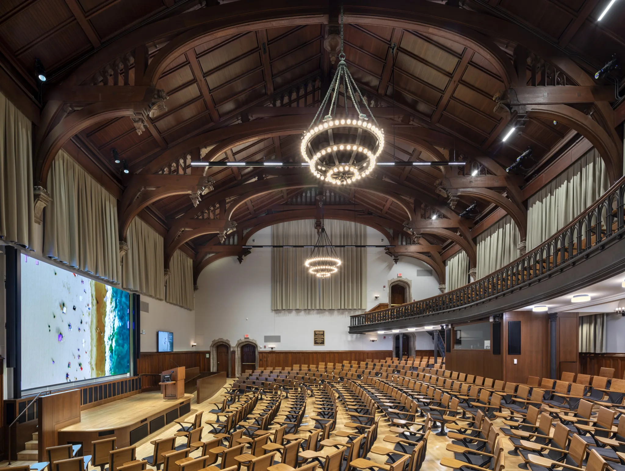 Princeton McCosh 50 lecture hall with timber trusses, chandeliers, curved seating, balcony, and large projection screen