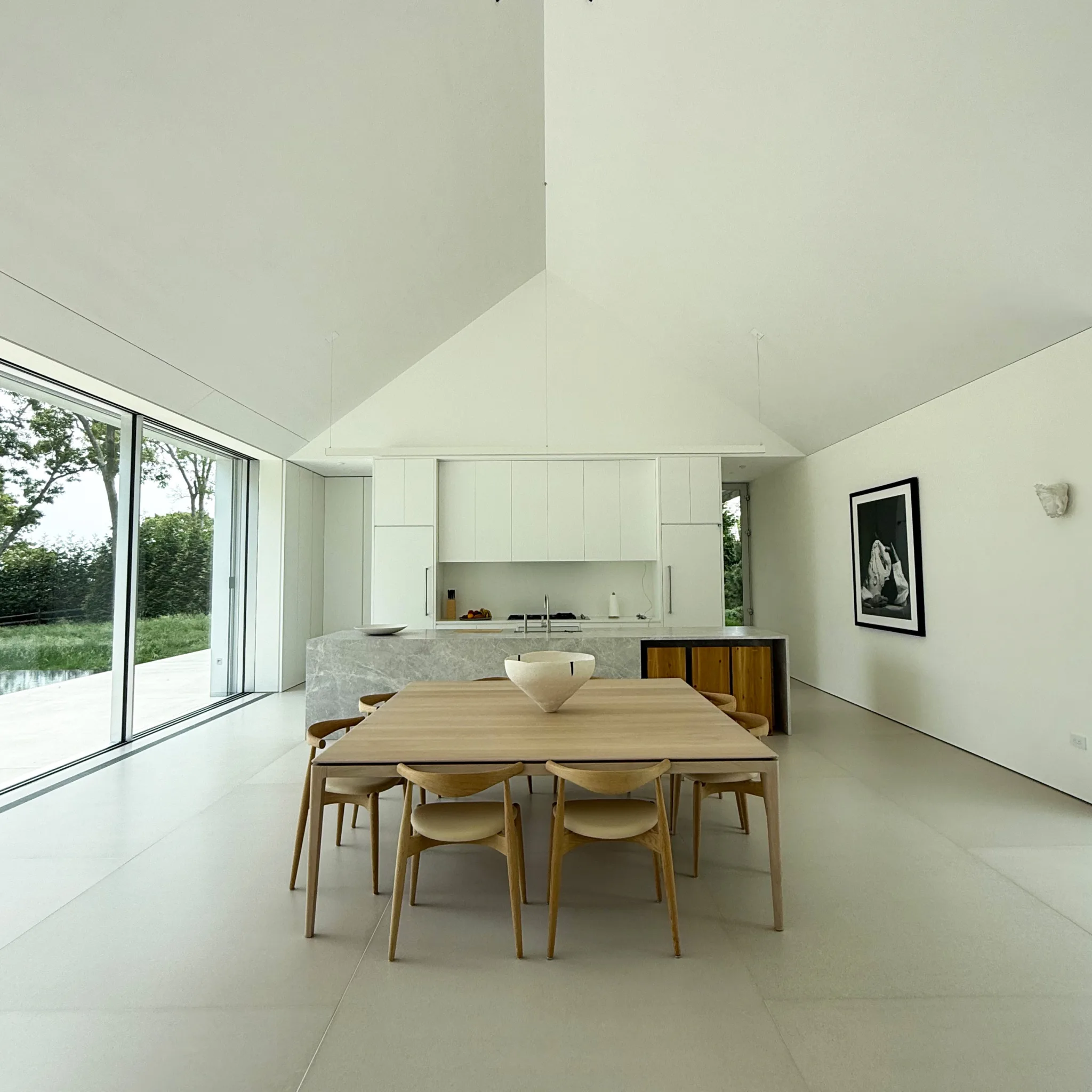 Bright, minimalist living and dining space in the Cedar Ave house, opening through wide glazing to views of Sag Harbor landscape.