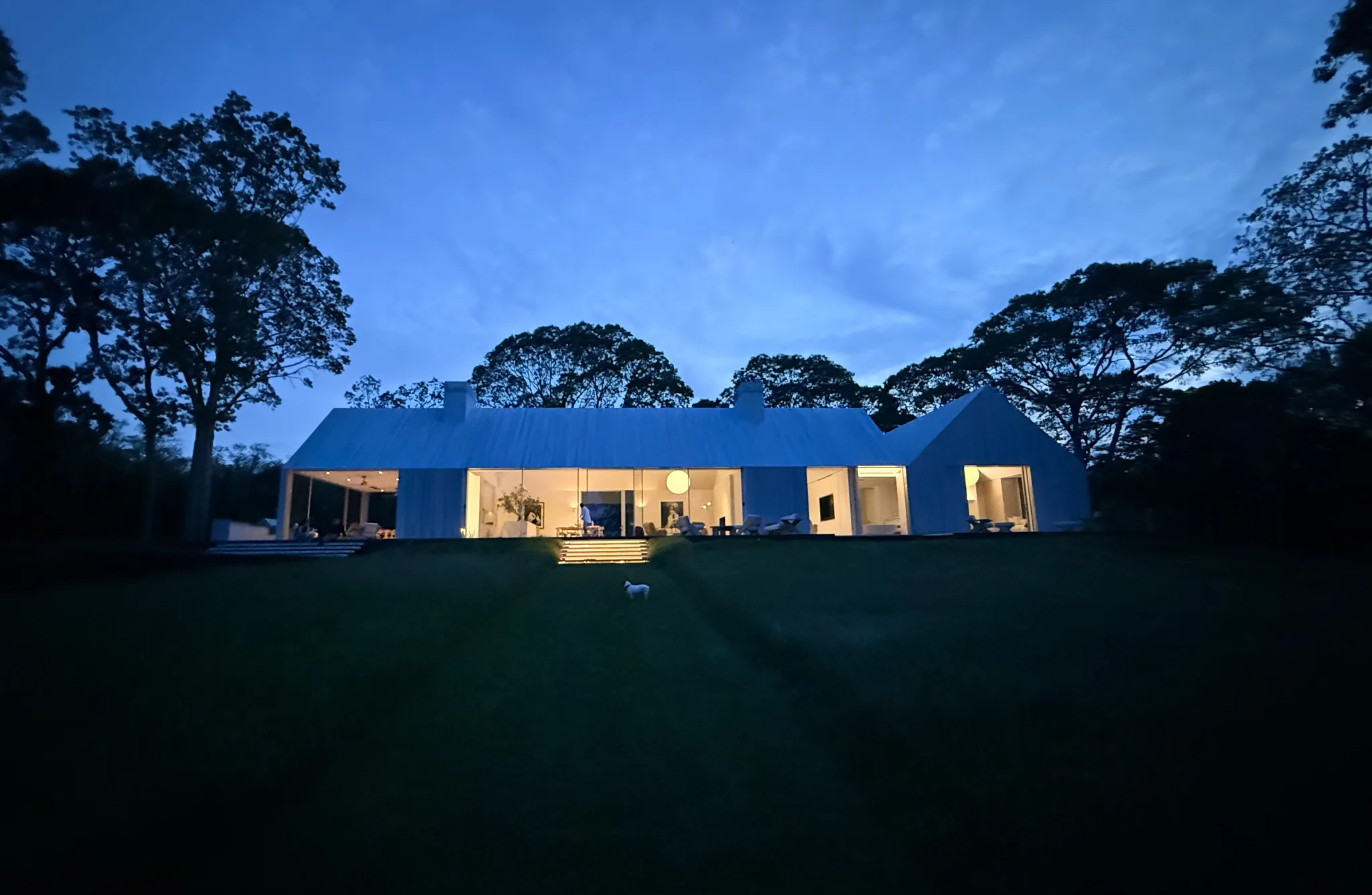 Evening view of the screened porch and glowing interiors of Kelly Klein’s Sag Harbor house, connecting indoor living to waterside landscape.