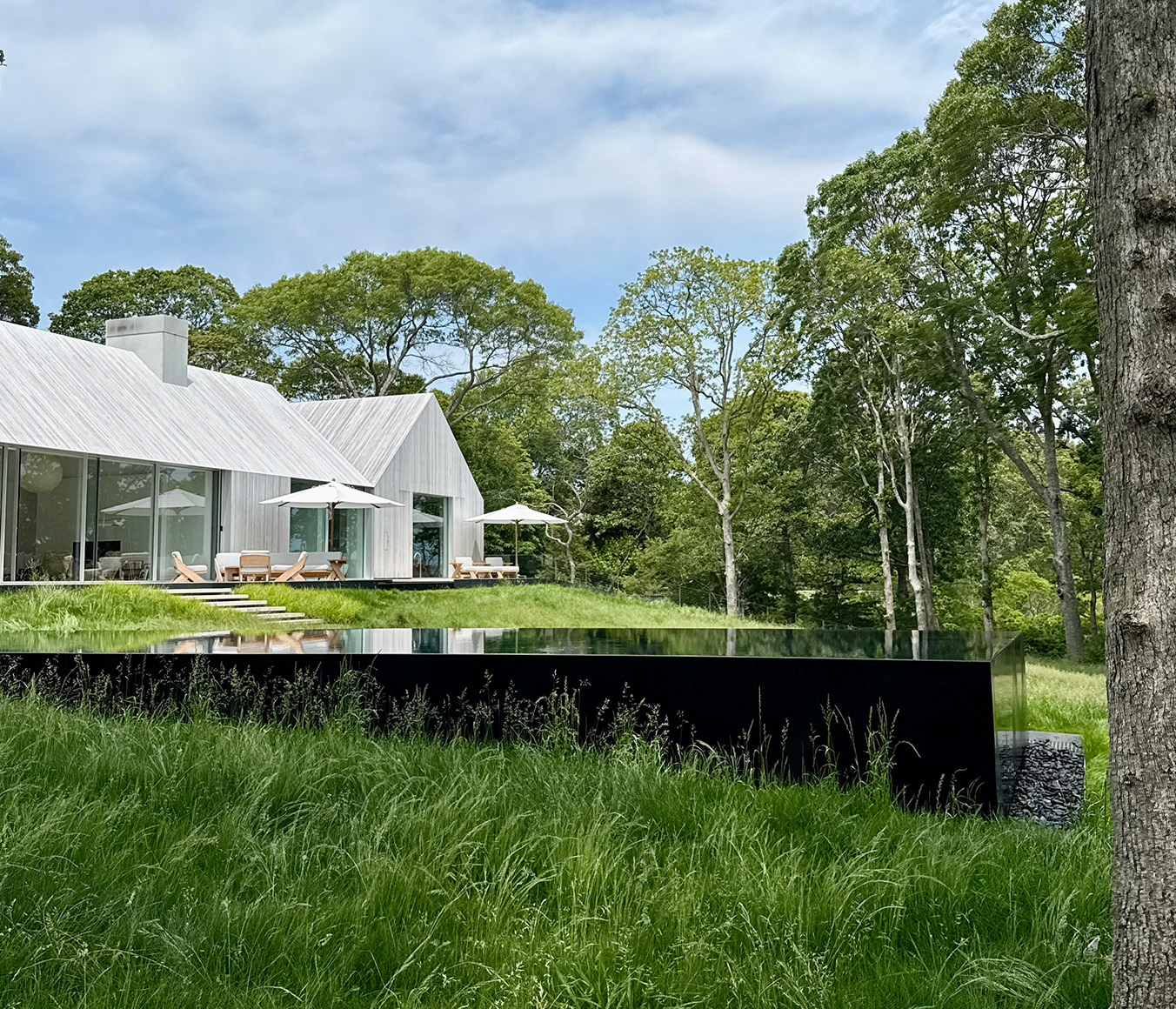 Sag Harbor waterfront house by 1100 Architect for Kelly Klein, featuring two perpendicular barn-like volumes and lush lawn leading to Sag Harbor Bay.