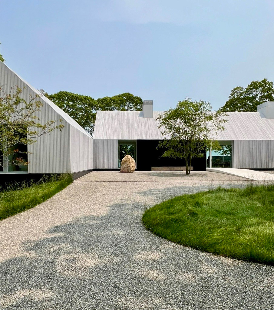 Modern residence in Sag Harbor designed by 1100 Architect, featuring gabled volumes clad in light vertical siding, large windows with trees and natural landscaping.