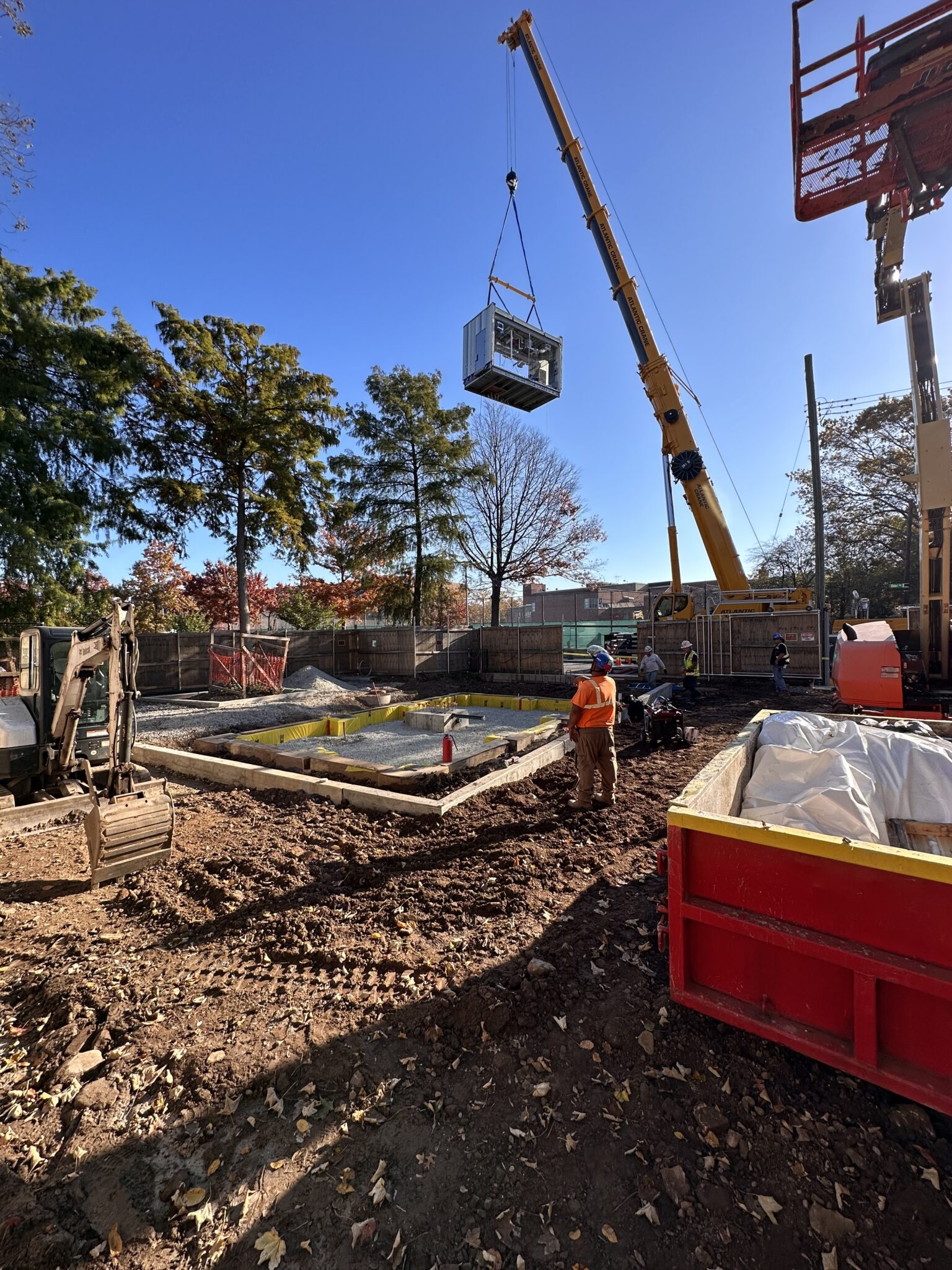 Crane lifting a prefabricated comfort station module into place at a park construction site, with workers guiding the installation.
