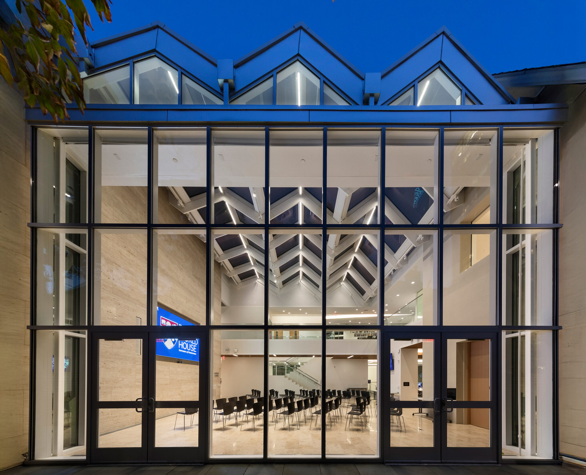 UPenn Perry World House glass façade with sawtooth skylights, showing event seating in the World Forum at dusk