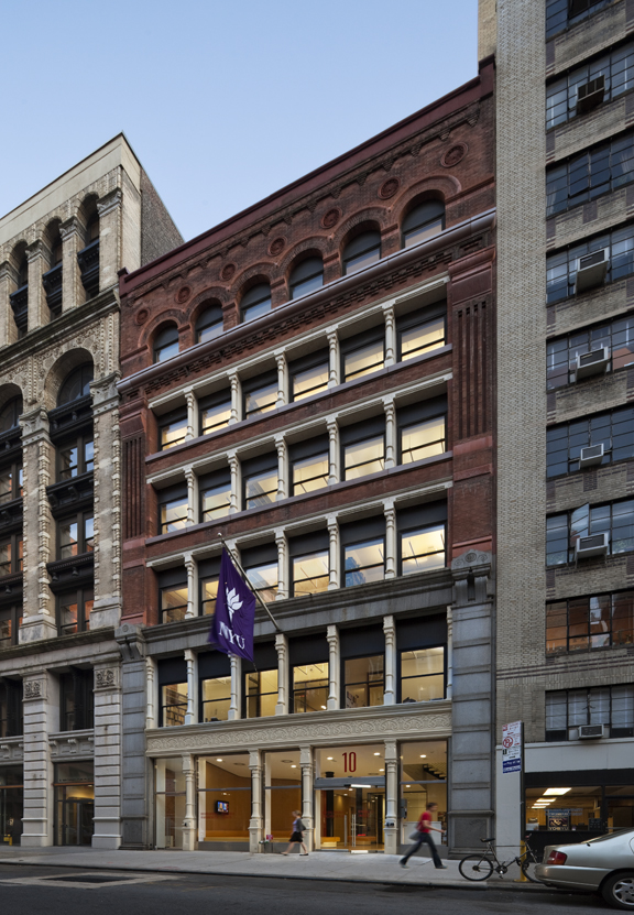 Restored historic façade of the NYU Department of Linguistics building, featuring red brick, arched upper windows, and an illuminated ground-floor entry.