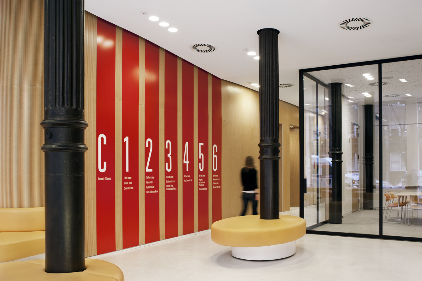 Lobby corridor with bold vertical signage and cylindrical black columns integrated into round upholstered seating.