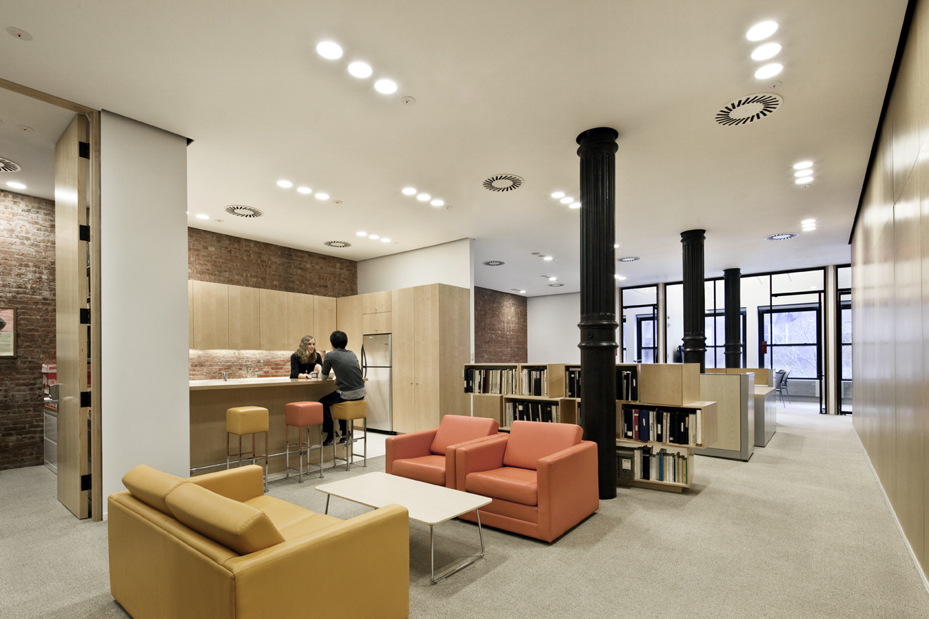 Flexible study and lounge space with warm-toned seating, wood cabinetry, and black structural columns contributing to the room’s character.