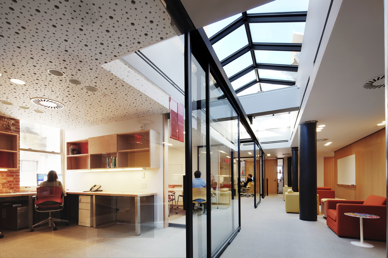 Daylit workspace with a skylit corridor, glass partitions, built-in desks, and a mix of open seating areas along the central atrium.