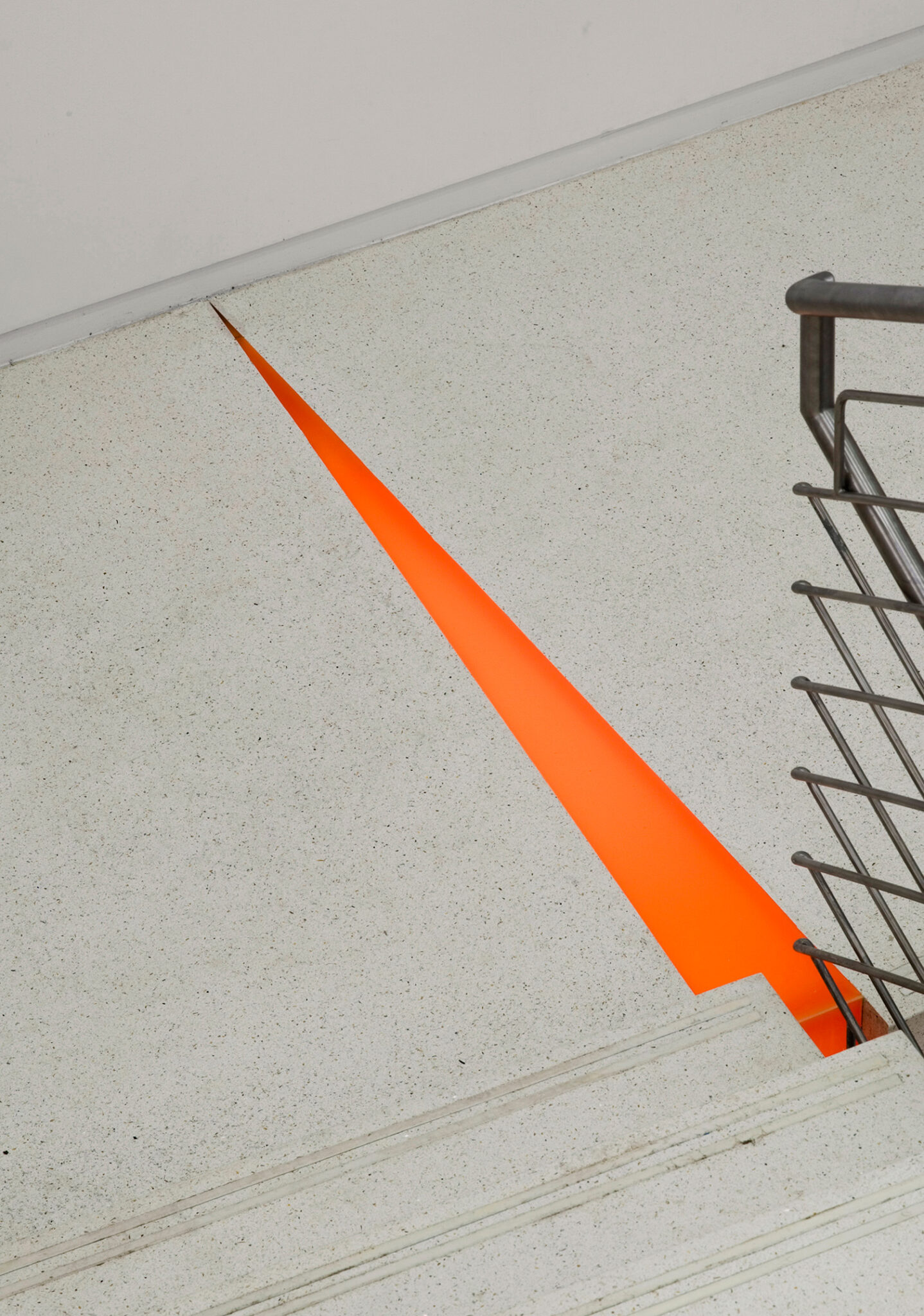 A central stair at The New School with terrazzo treads, stainless-steel railings, and accents of orange seating below, connecting two bright, open lobby levels.