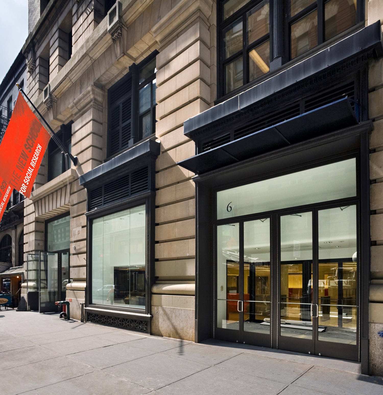 Street-level exterior of The New School entrance at 6 East 16th Street, showcasing large storefront windows and the university’s red banner.