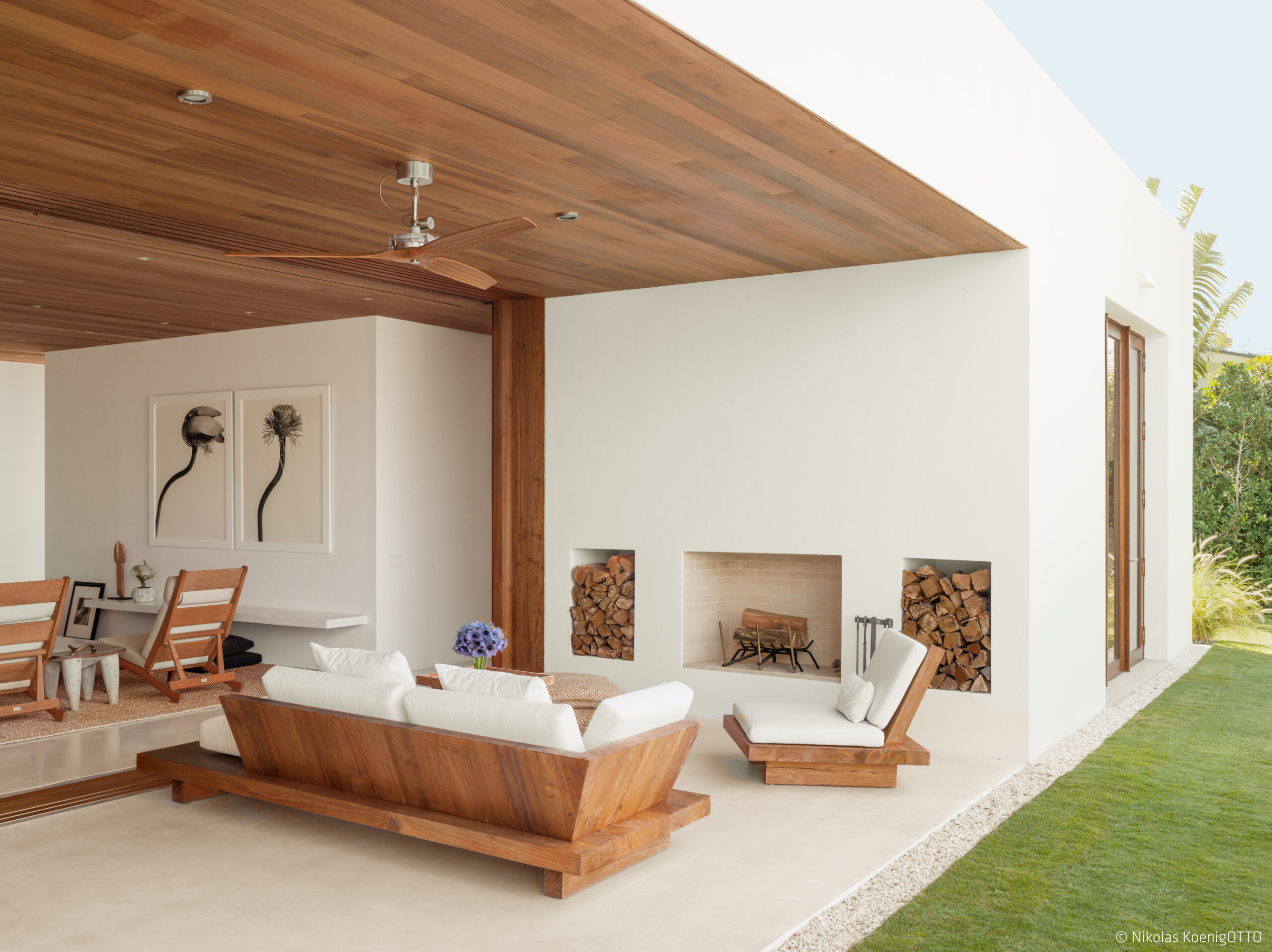 Outdoor living space with teak furniture, covered patio, and built-in fireplace blending indoor and outdoor comfort.