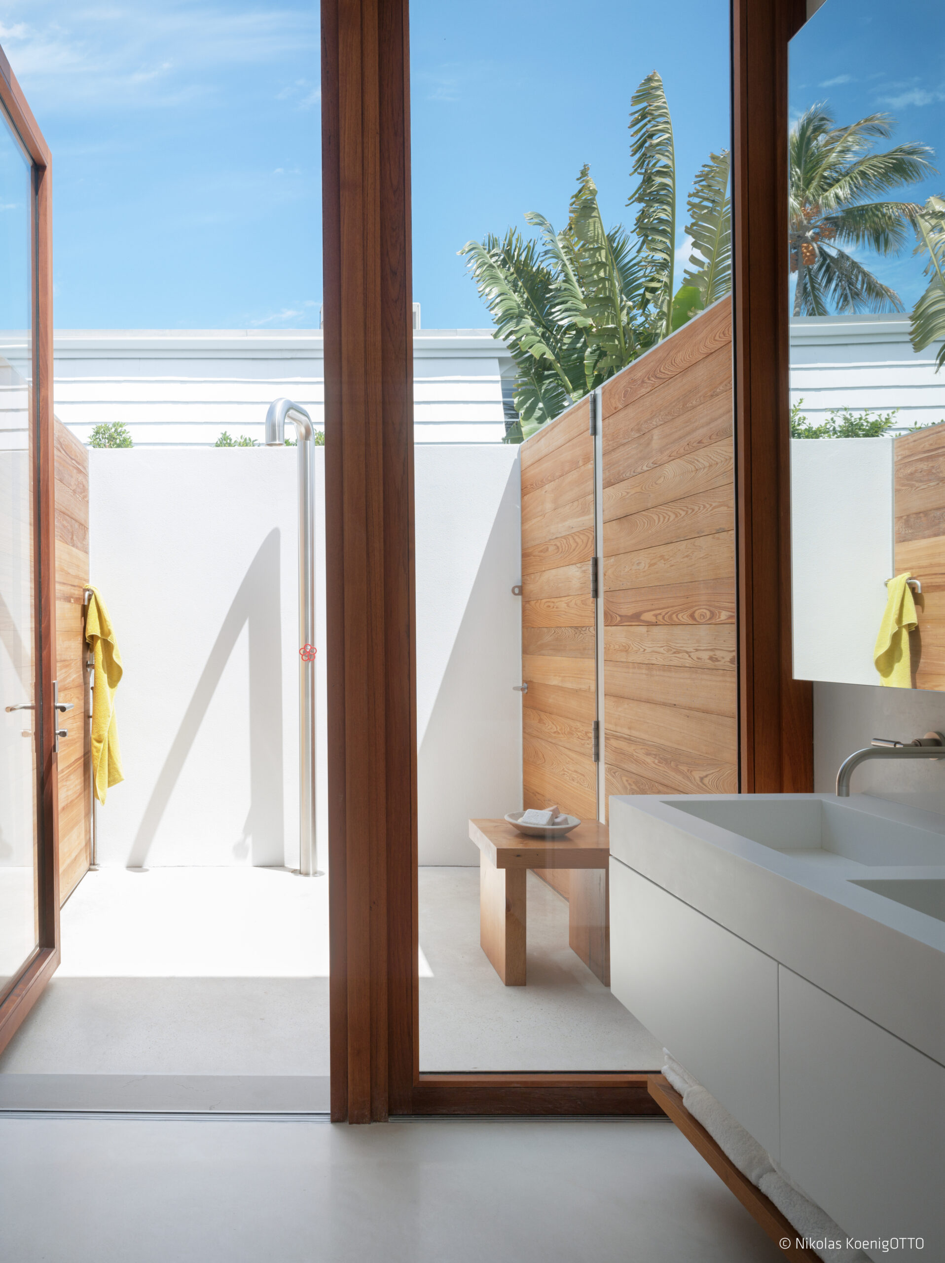 Minimalist bathroom with outdoor shower enclosed by wood privacy screens and tropical garden backdrop.