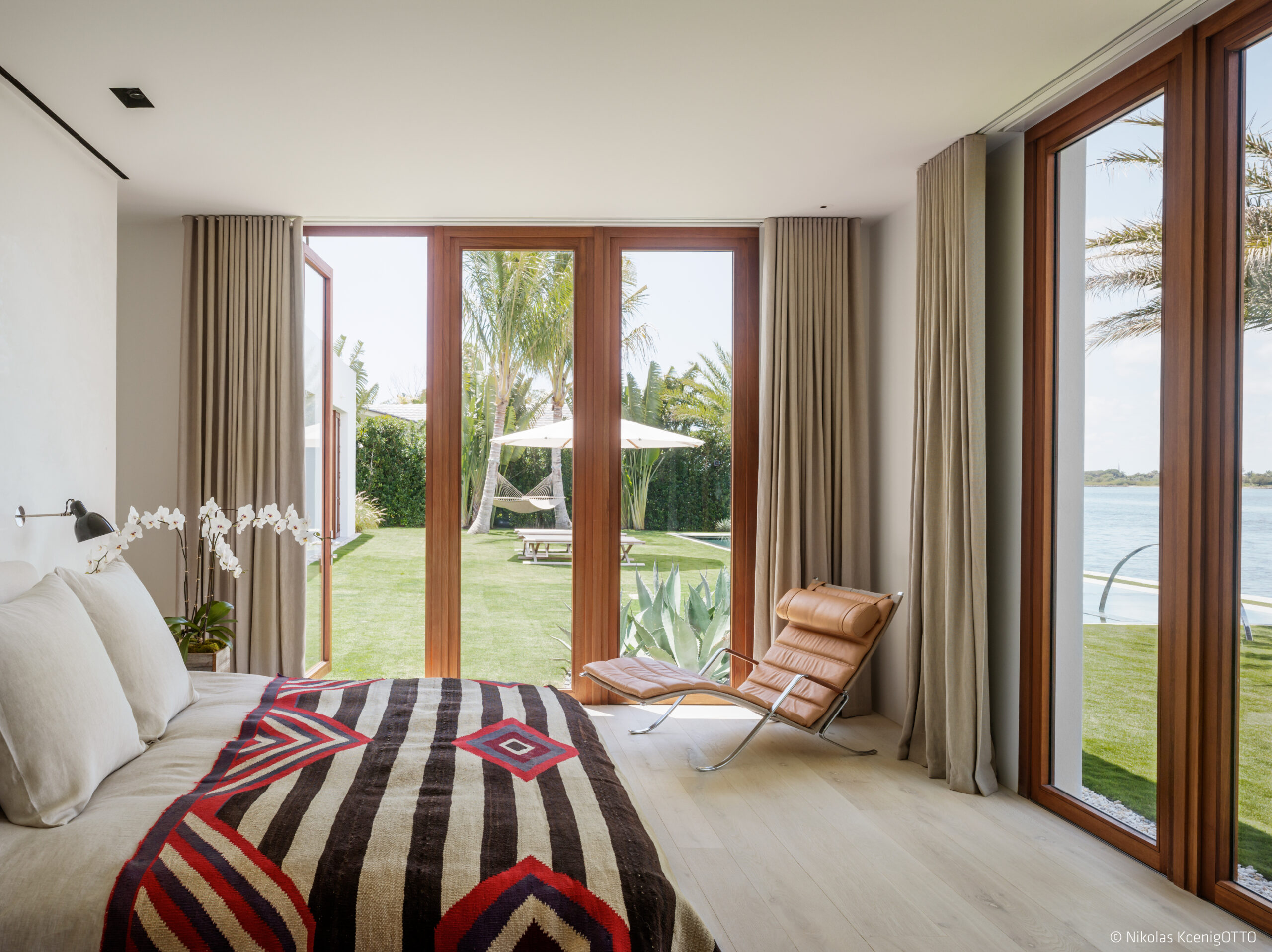 Bedroom with floor-to-ceiling windows and terrace access, featuring views of the pool and waterfront landscape.