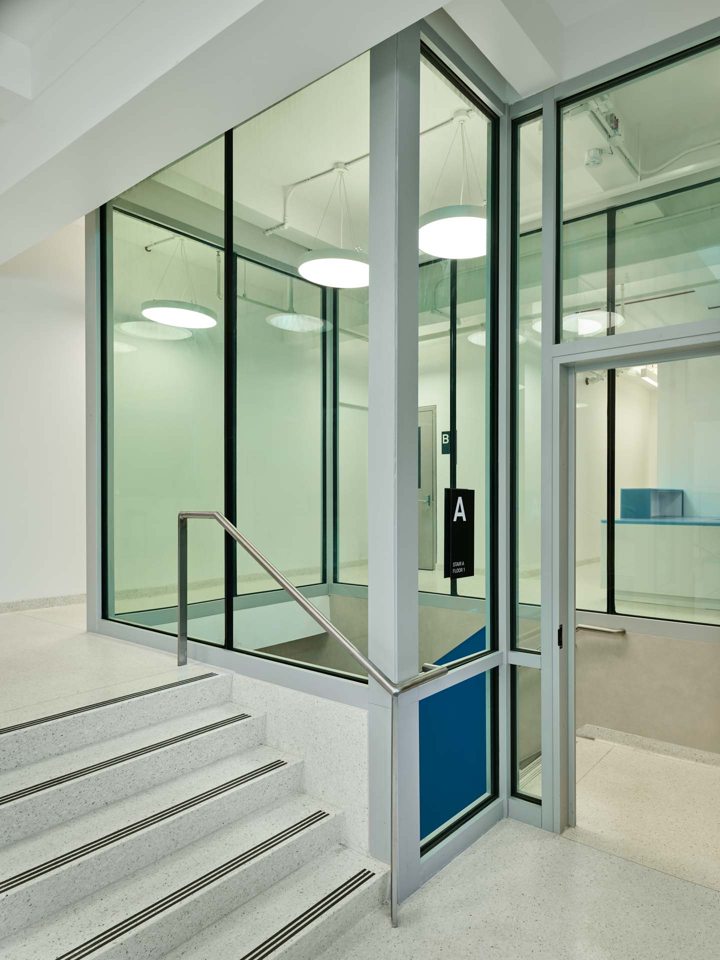 Glass-enclosed stair vestibule with terrazzo steps and blue accent panel in renovated NYC civic recreation facility.