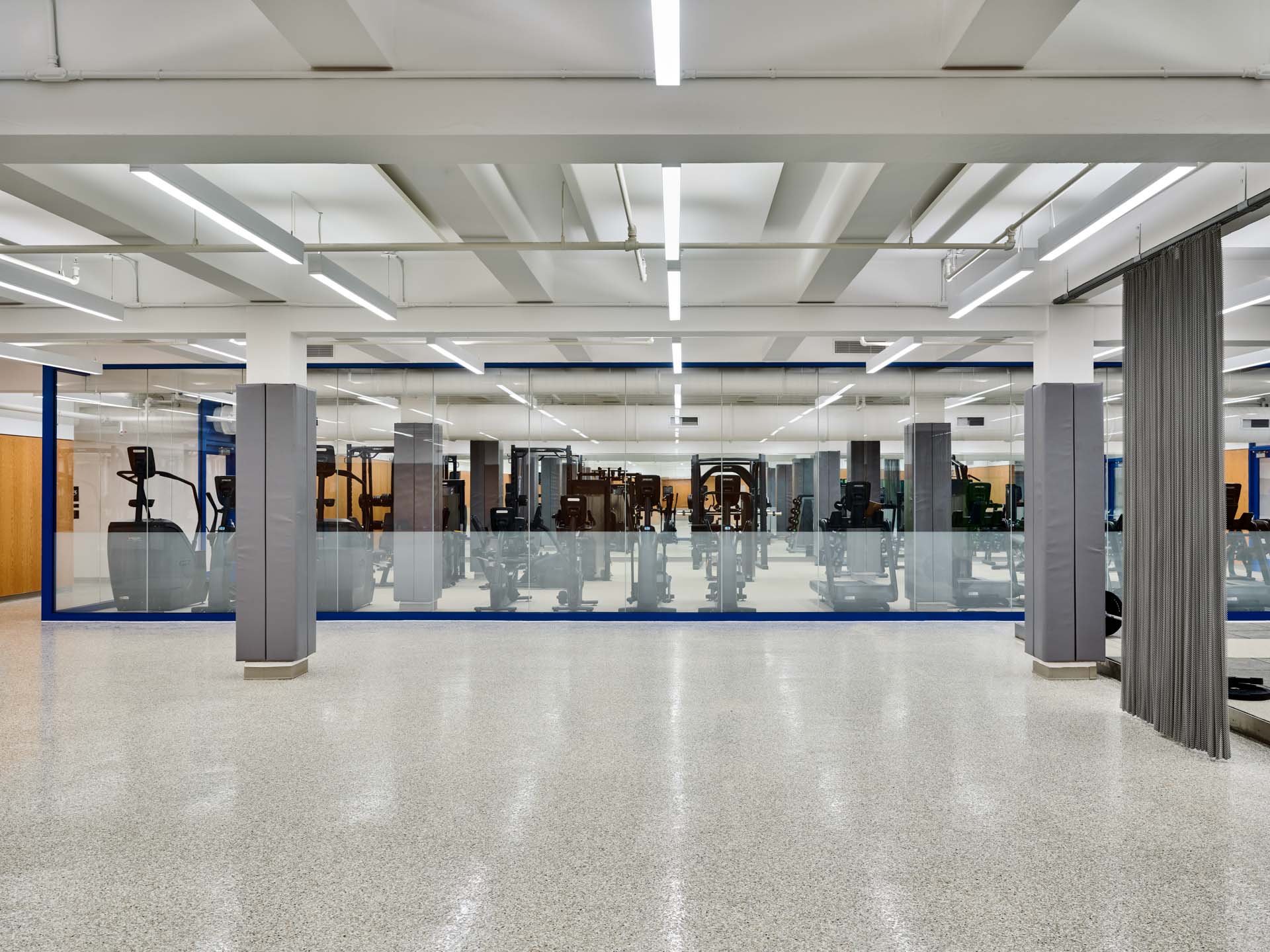 Open fitness floor with terrazzo flooring, glass partition walls, and cardio equipment in renovated NYC Parks recreation center.