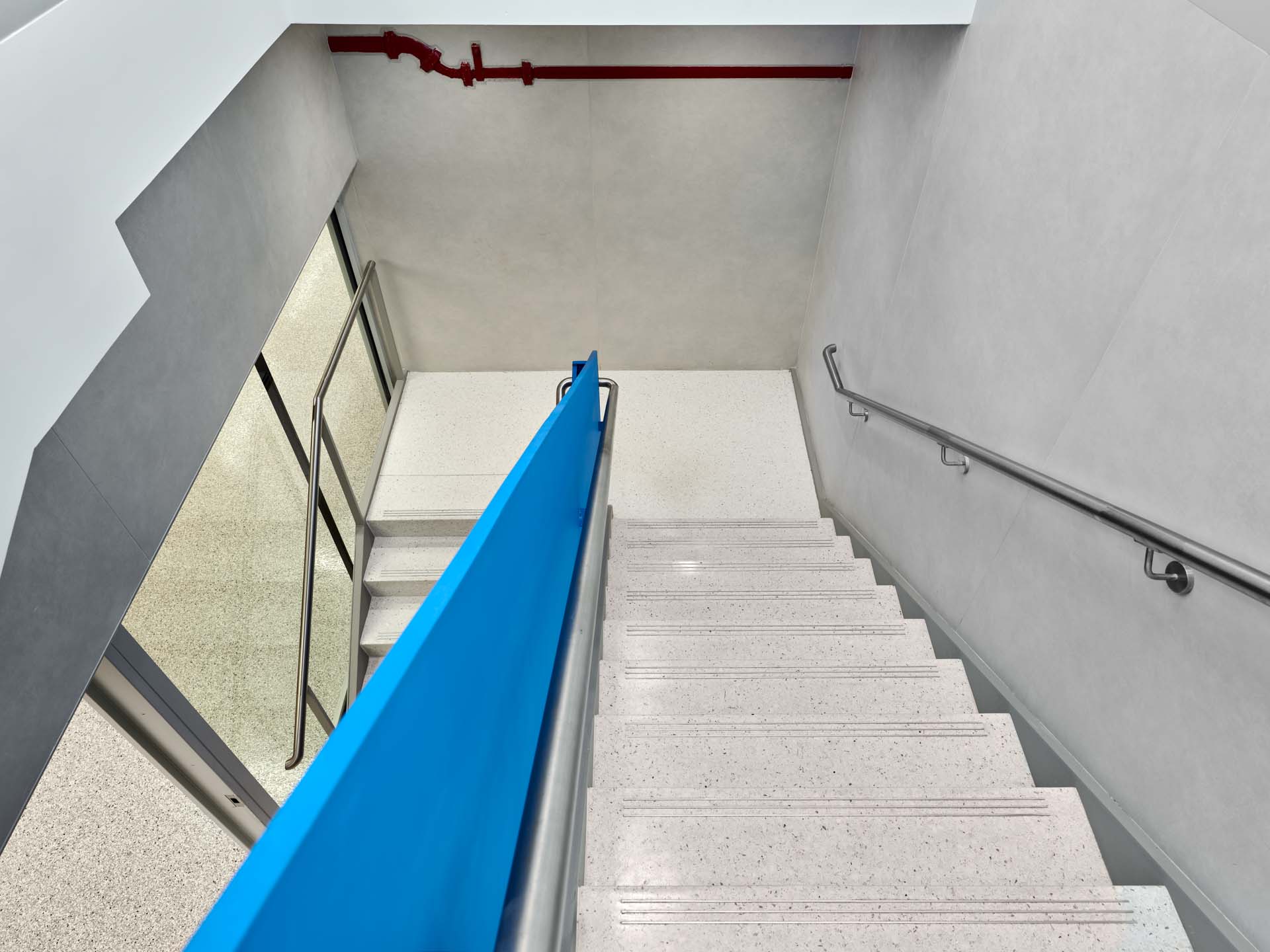 Looking down terrazzo stair with blue painted stringer and stainless steel handrail in NYC civic facility renovation.